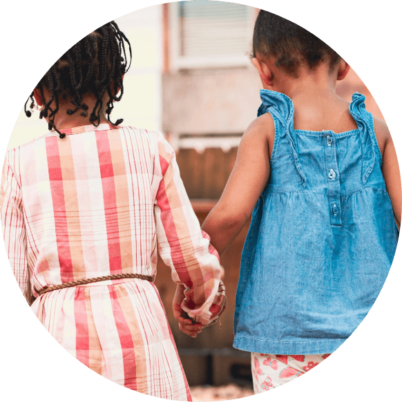 photograph of girl with patterned orange and white dress holding hands with a smaller girl with blue denim dress